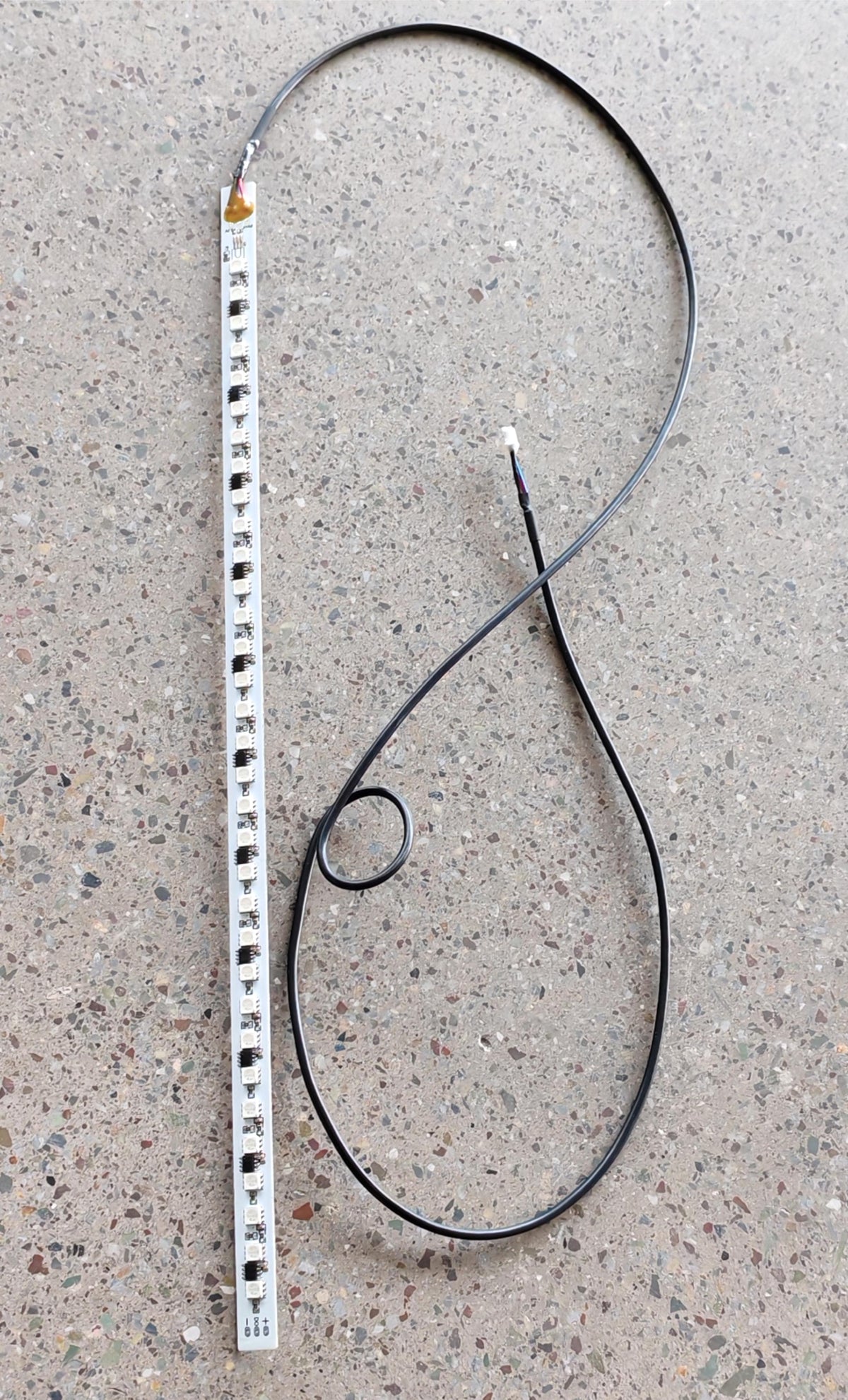 Barre LED flexible blanche reliée à un long câble noir sur fond moucheté